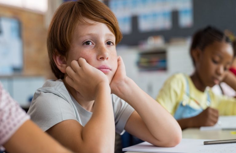 Young male student resting his head on his hands from boredom in class.